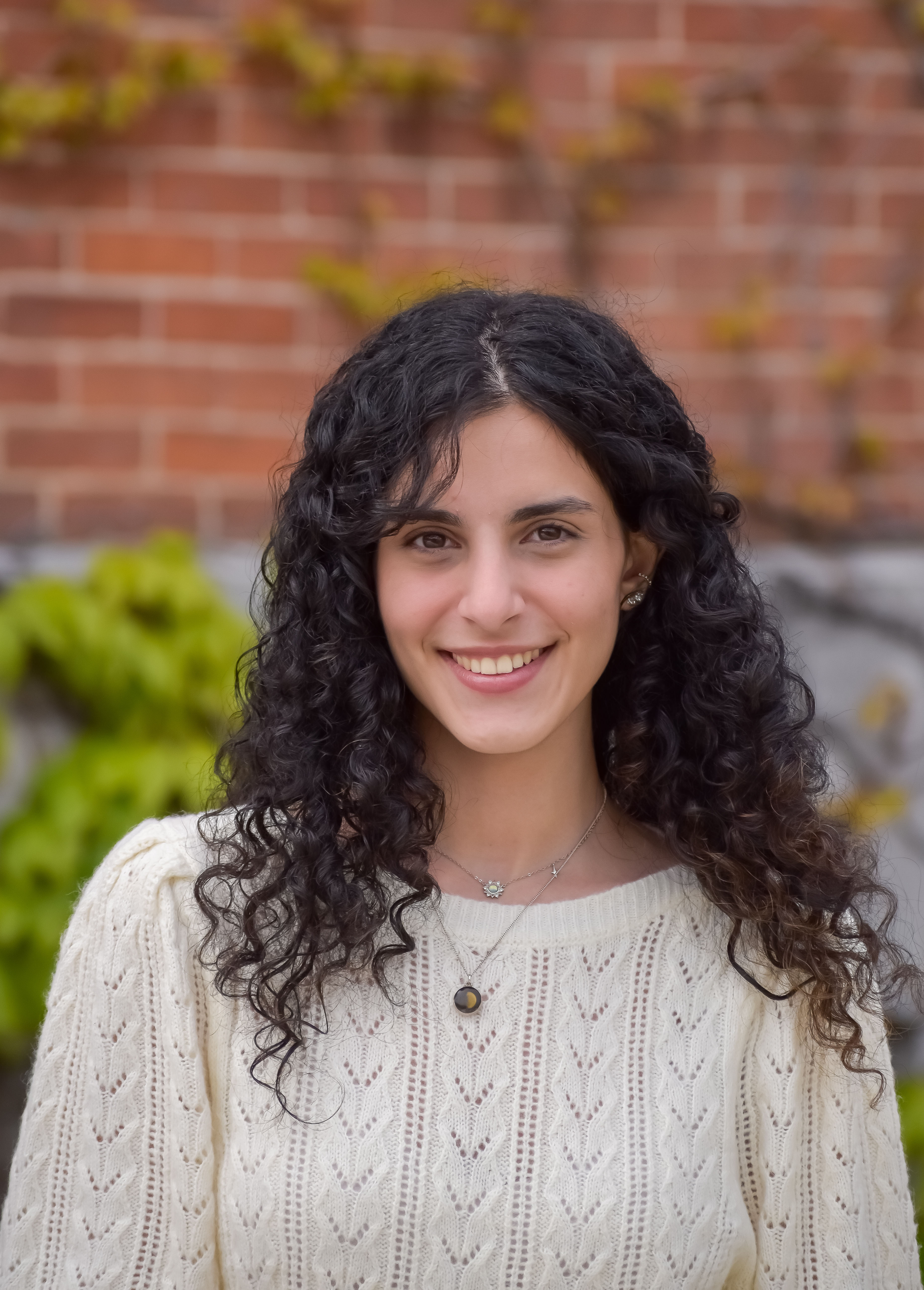 Headshot of Zahraa Abdul Hasan in front of a background of blurred out red brick.