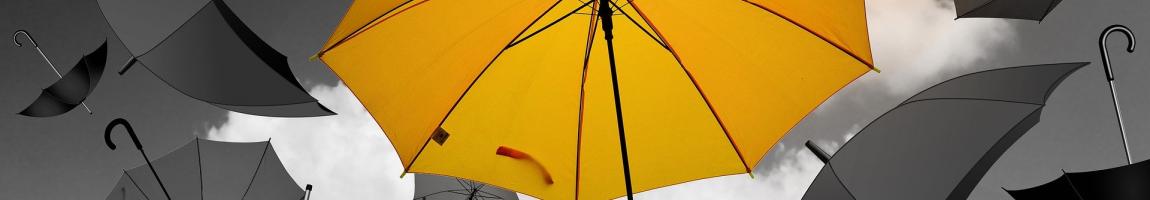 A yellow umbrella floats in front of multiple other grey umbrellas.