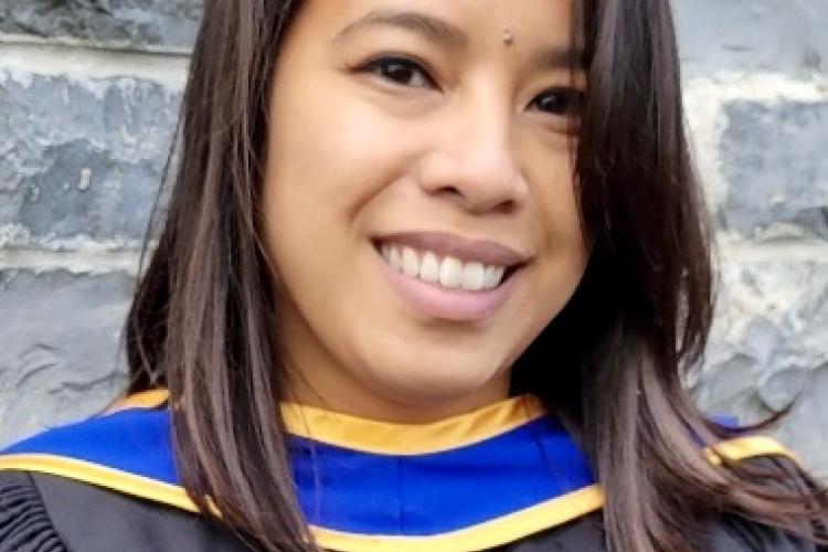 Headshot photo of Pearl Esquivel wearing a black graduation gown with blue and yellow convocation hood.